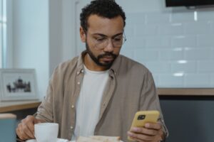 Man met kop koffie die op telefoon kijkt