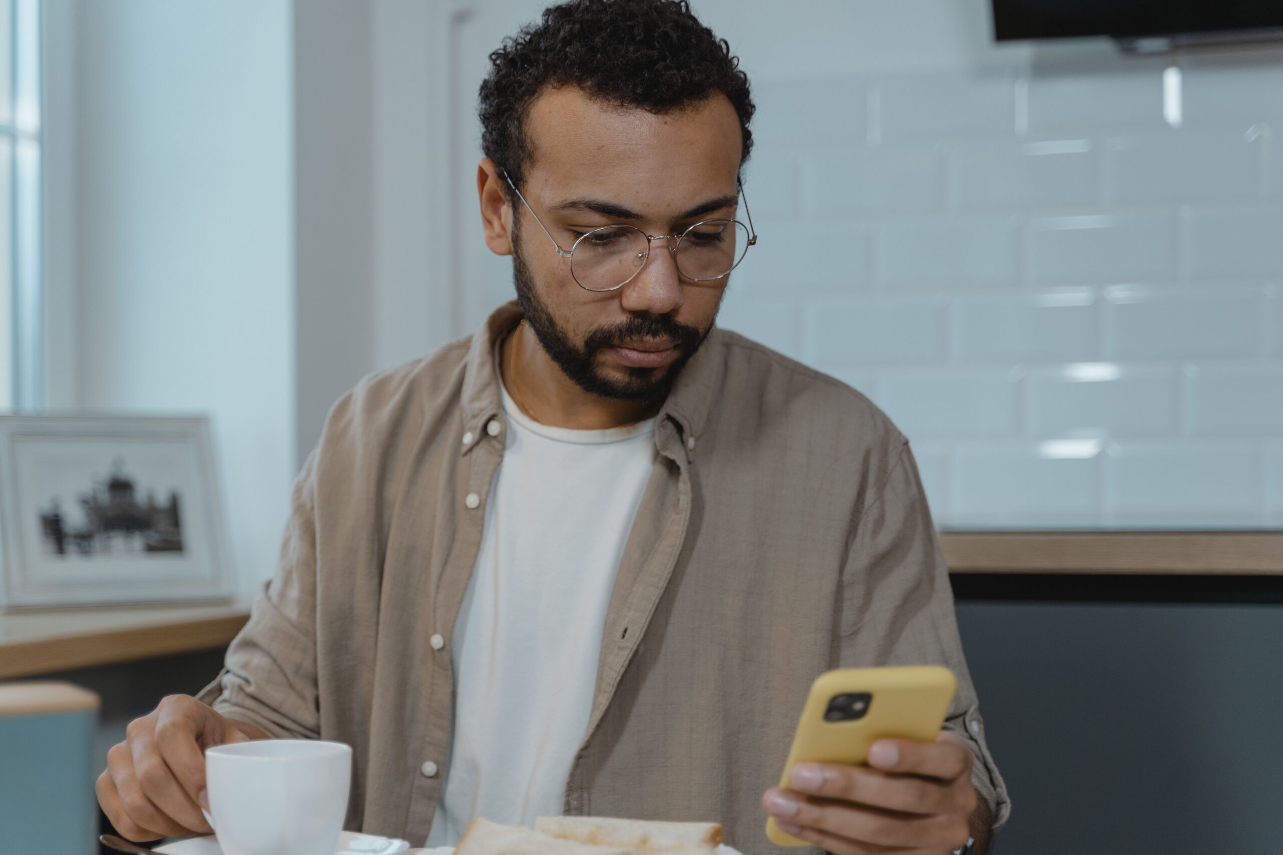 Man met kop koffie die op telefoon kijkt